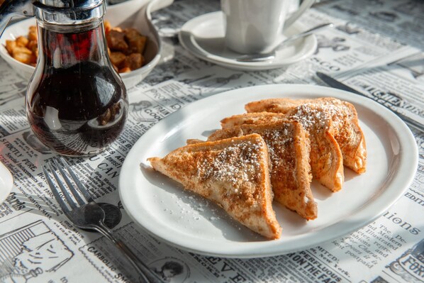 A plate of triangular pastries on a newspaper-covered table with a cup and a bottle.