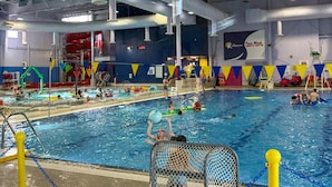 An indoor swimming pool with multiple lanes, a diving board, and a lifeguard stand.