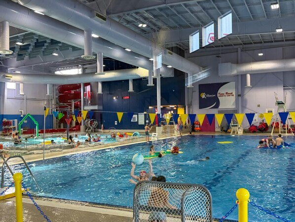 An indoor swimming pool with multiple lanes, a diving board, and a lifeguard stand.