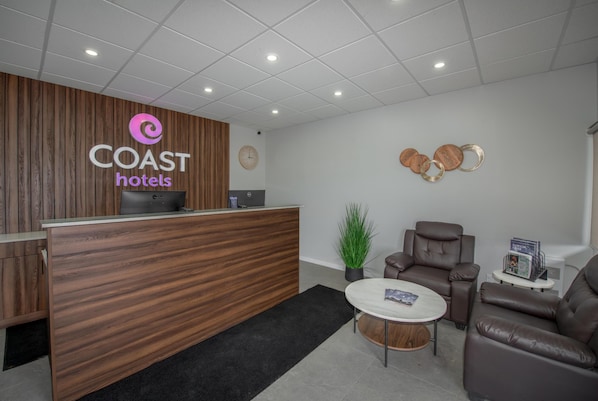 A reception desk with a wooden finish, a clock, a potted plant, leather seating, and a small table with magazines.