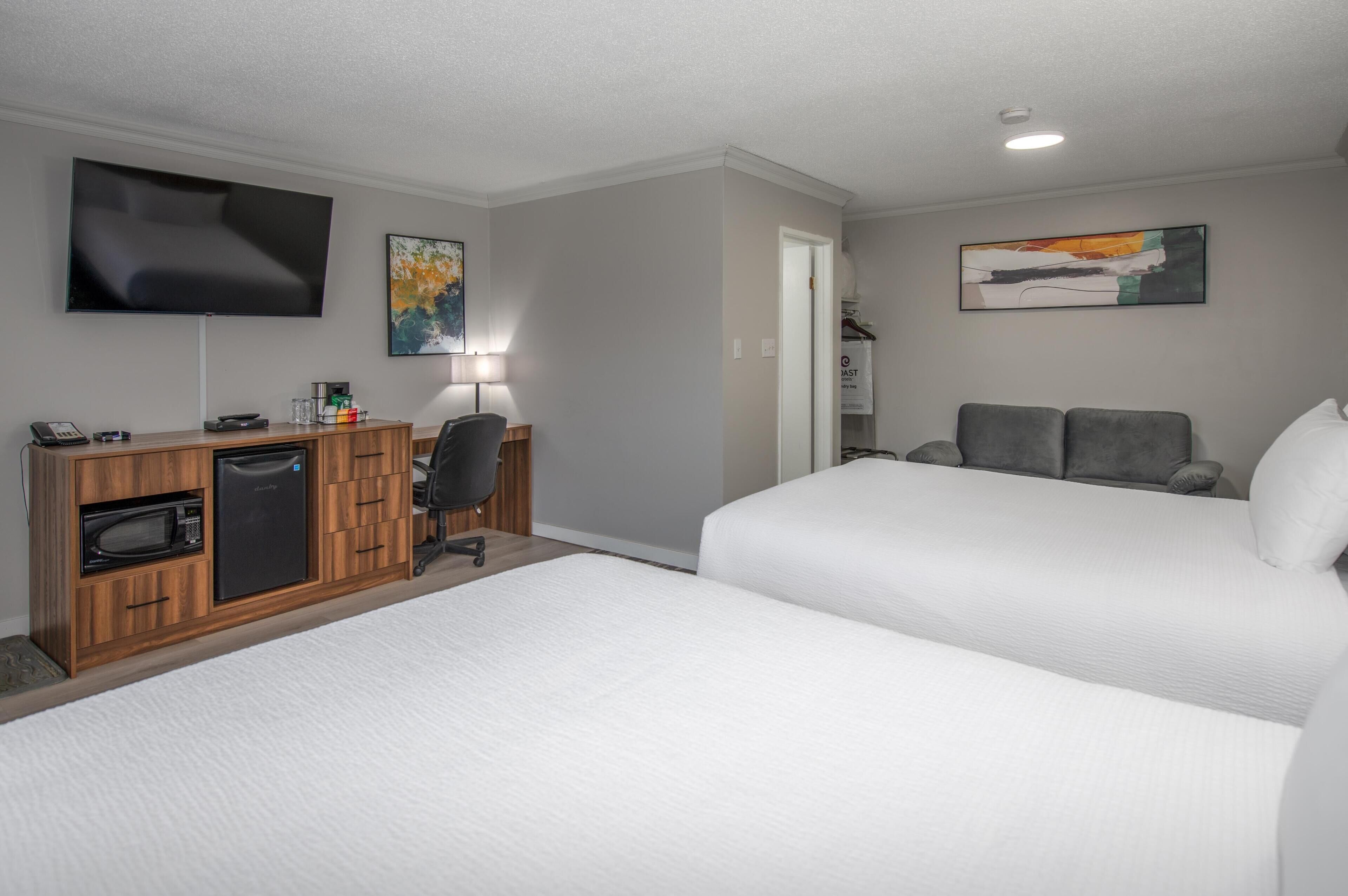A hotel room with two beds, a desk with a microwave, a TV, and a cabinet.