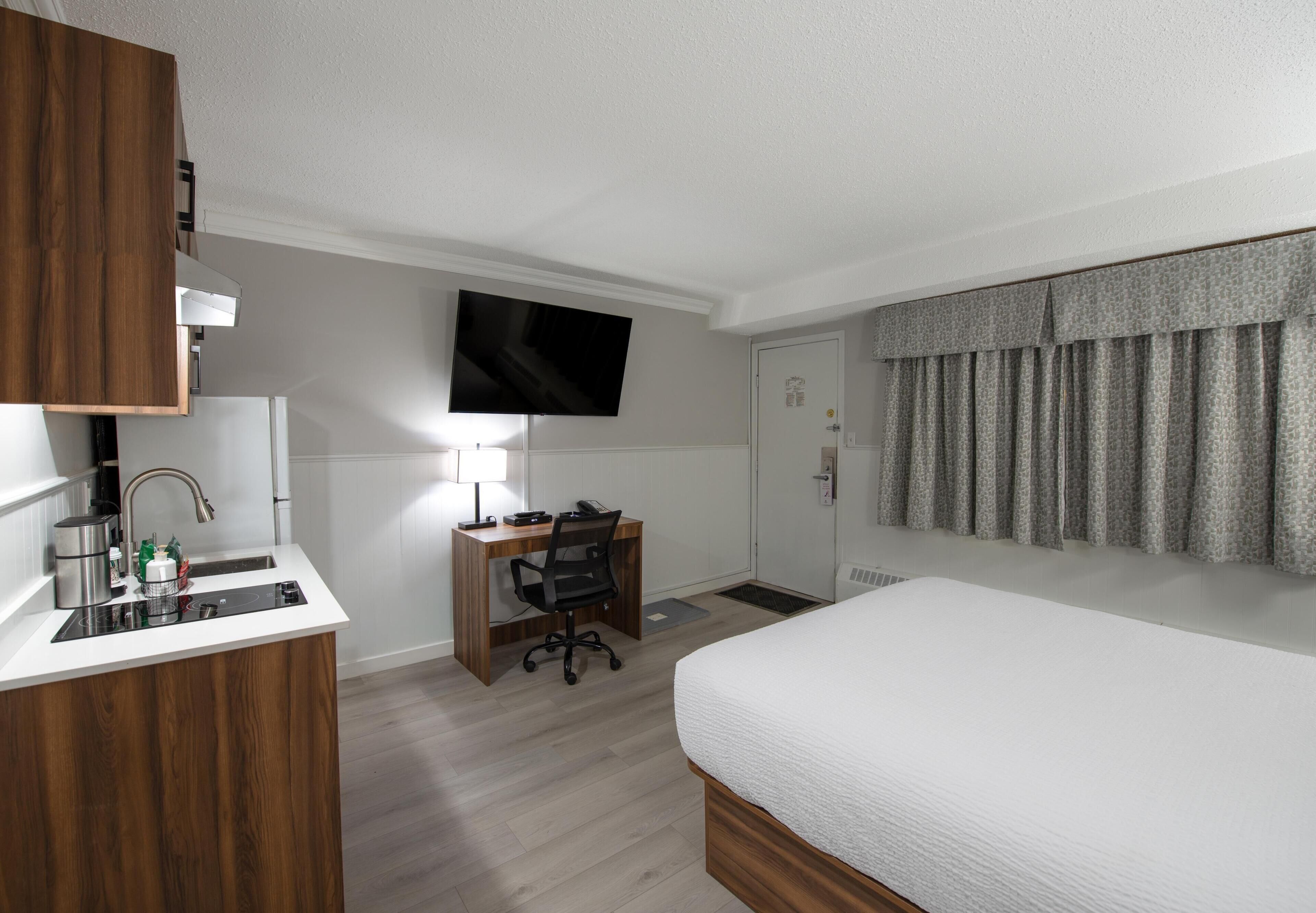 Ein Hotelzimmer mit einem Bett, einem Schreibtisch mit Stuhl, einem an der Wand montierten Fernseher und einer Badezimmertür.