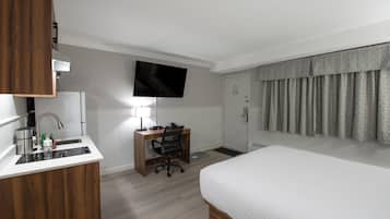 Ein Hotelzimmer mit einem Bett, einem Schreibtisch mit Stuhl, einem an der Wand montierten Fernseher und einer Badezimmertür.