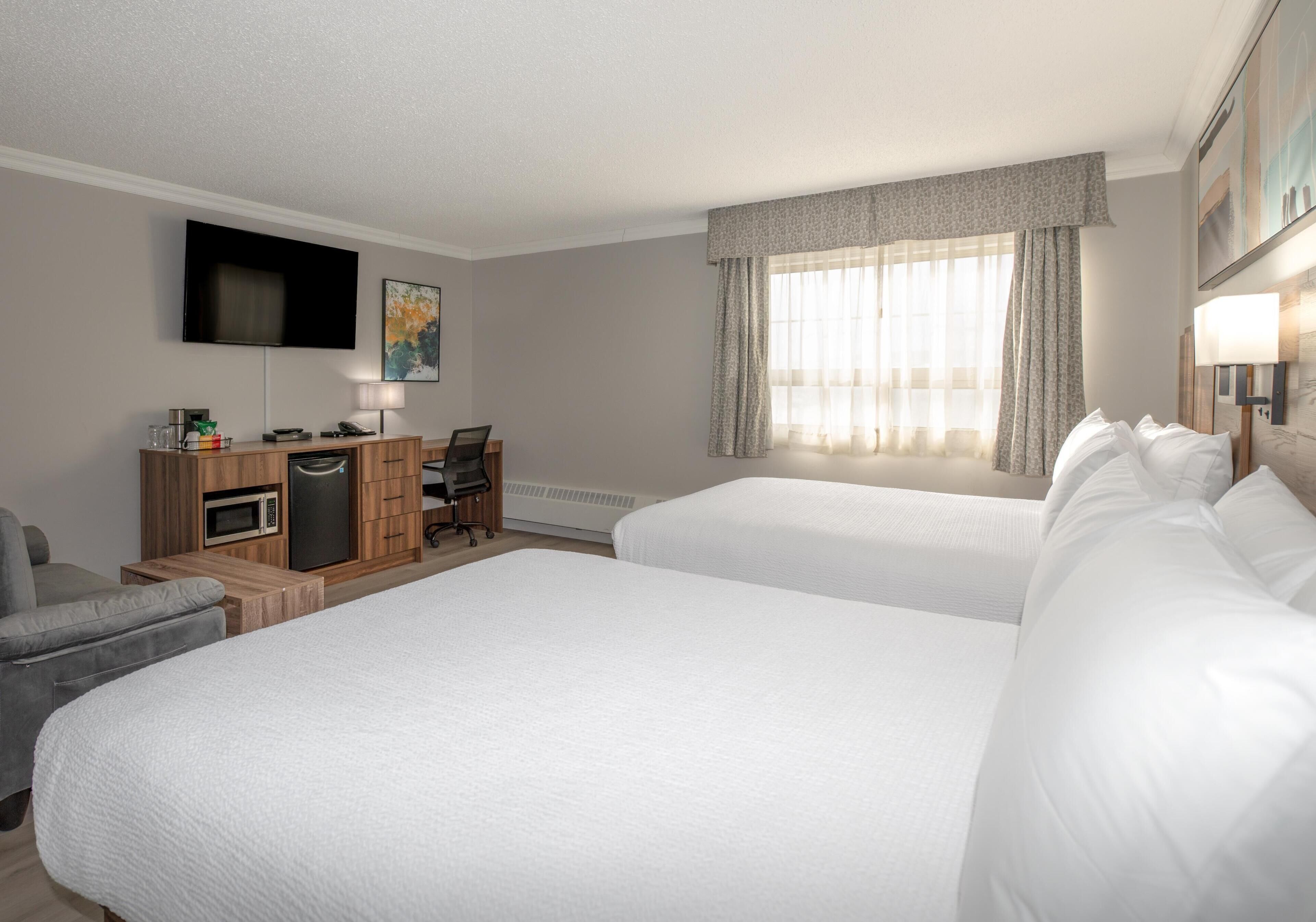 A hotel room with two beds, a desk with a computer, a TV, and a window with curtains.