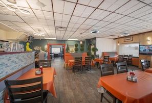 Un restaurant avec plusieurs tables et chaises, un comptoir avec une enseigne et un plafond doté d’un éclairage encastré.