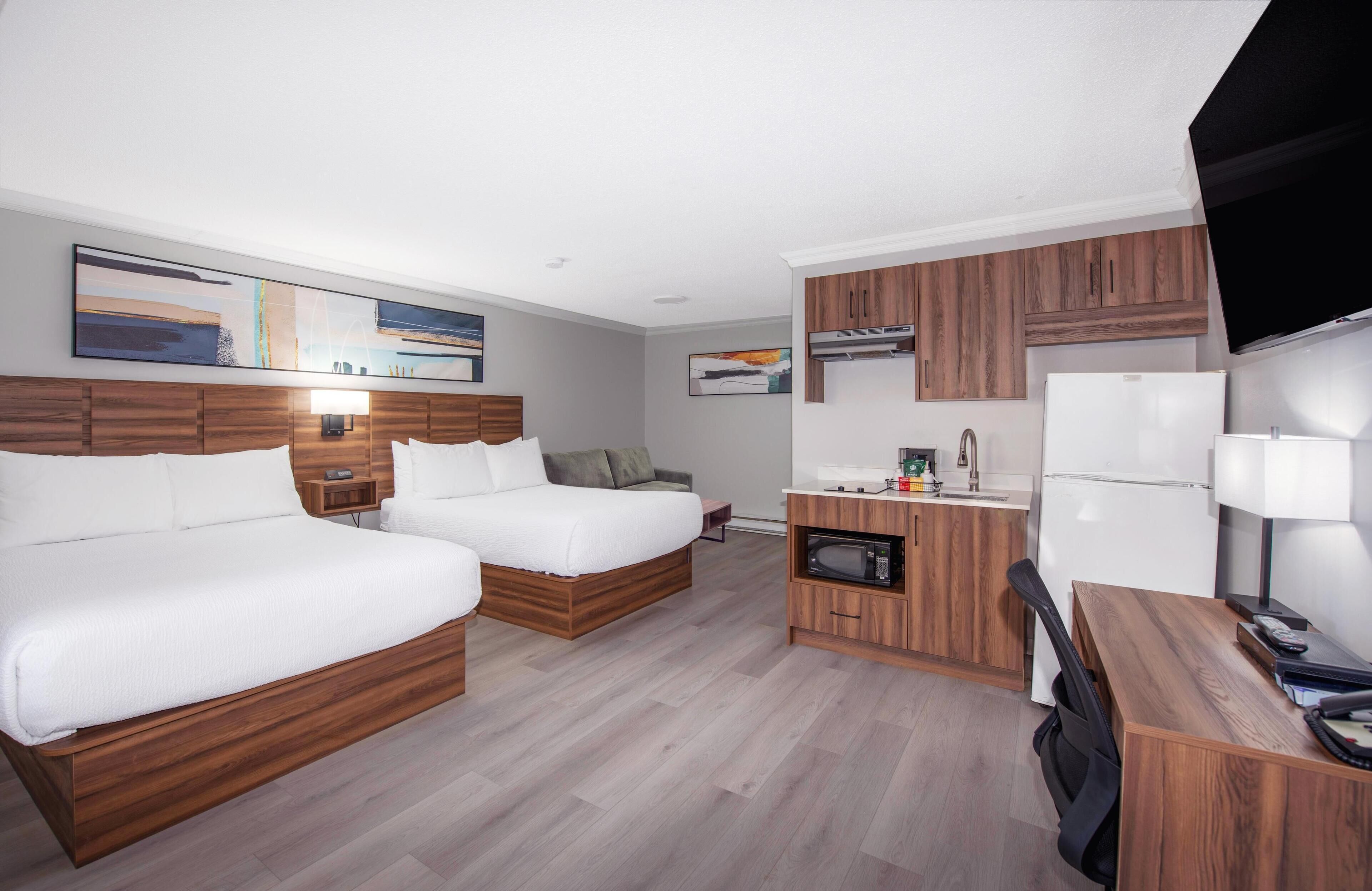 A hotel room with two beds, a kitchenette, and a flat-screen TV.