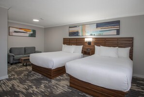 Una habitación de hotel con dos camas, un sofá, una mesita de noche y obras de arte en las paredes.