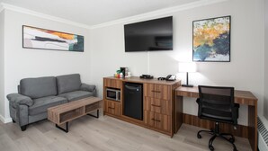 A compact living space with a sofa, a kitchenette, a flat-screen TV, and a desk with a chair.