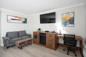 Un espace de vie compact comprenant un canapé, une kitchenette, un téléviseur à écran plat et un bureau avec une chaise.