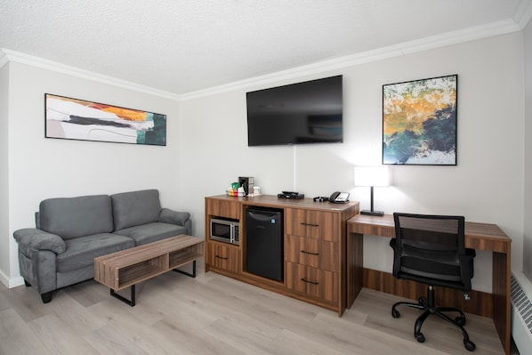 A compact living space with a sofa, a kitchenette, a flat-screen TV, and a desk with a chair.