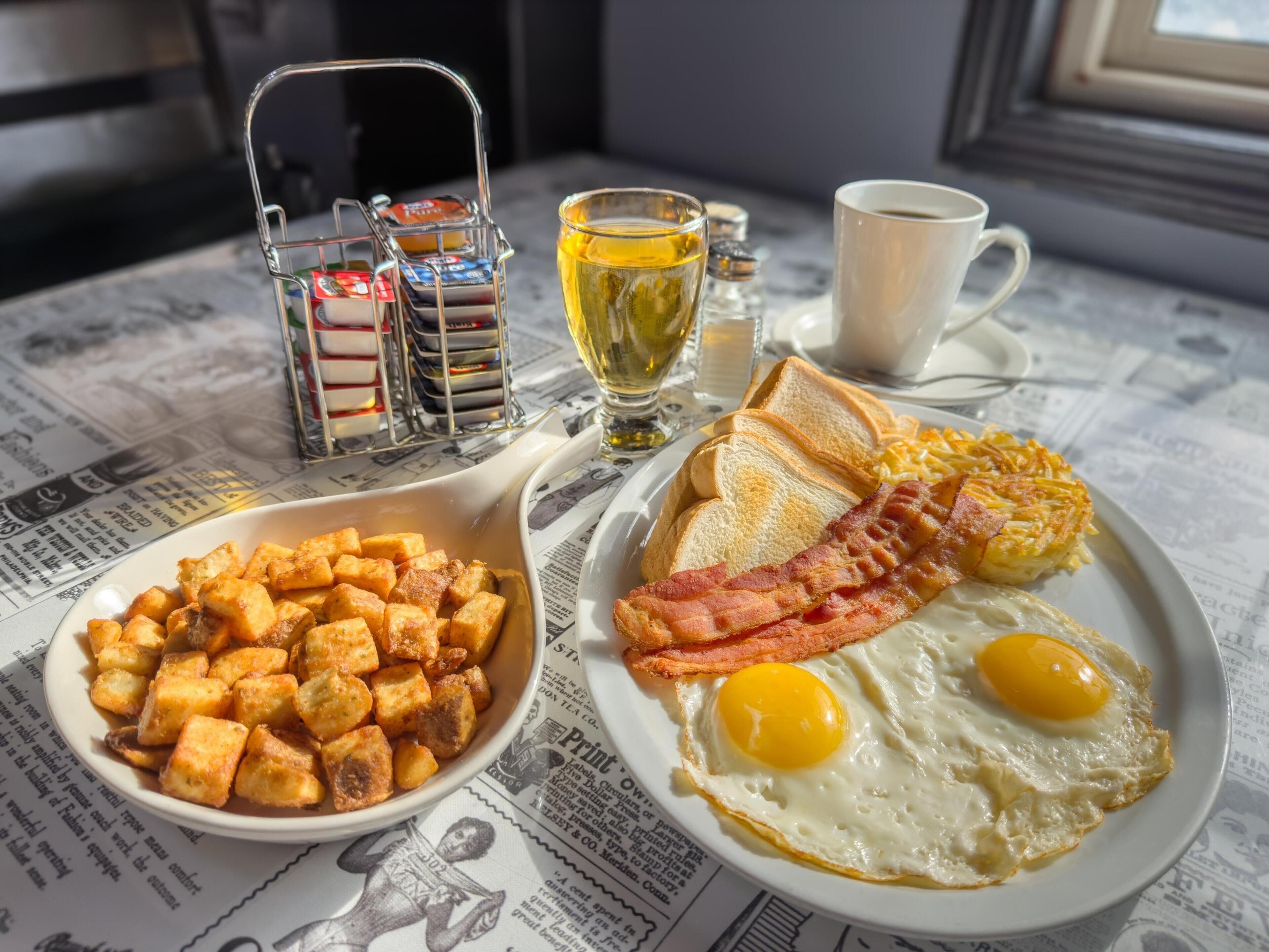 Un piatto per la colazione con uova, pancetta, toast e patate tritate su un tavolo ricoperto di giornale.