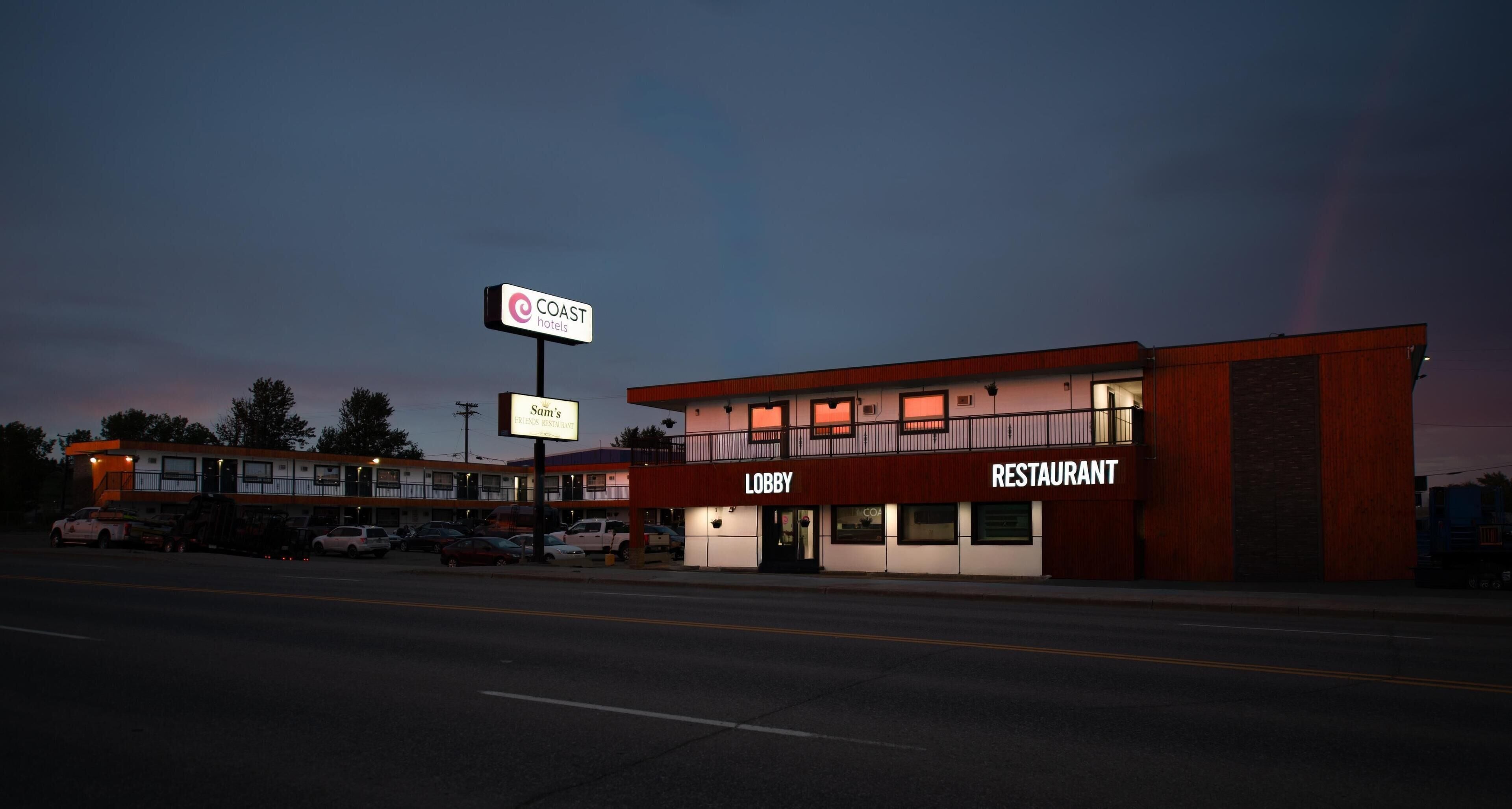Een gebouw met twee verdiepingen, met een bord voor 'COAST Hotels' en 'Sam's Friendly Restaurant' op de begane grond.