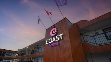 Une enseigne d’hôtel avec l’inscription « COAST hotels », une façade en bois et un parking avec des voitures.
