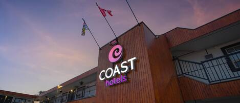 A hotel sign with 'COAST hotels' written on it, a wooden facade, and a parking area with cars.