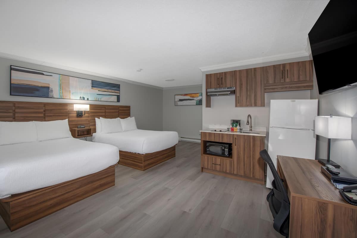 Habitación de hotel con dos camas, kitchenette, televisor de pantalla plana y obras de arte en las paredes.