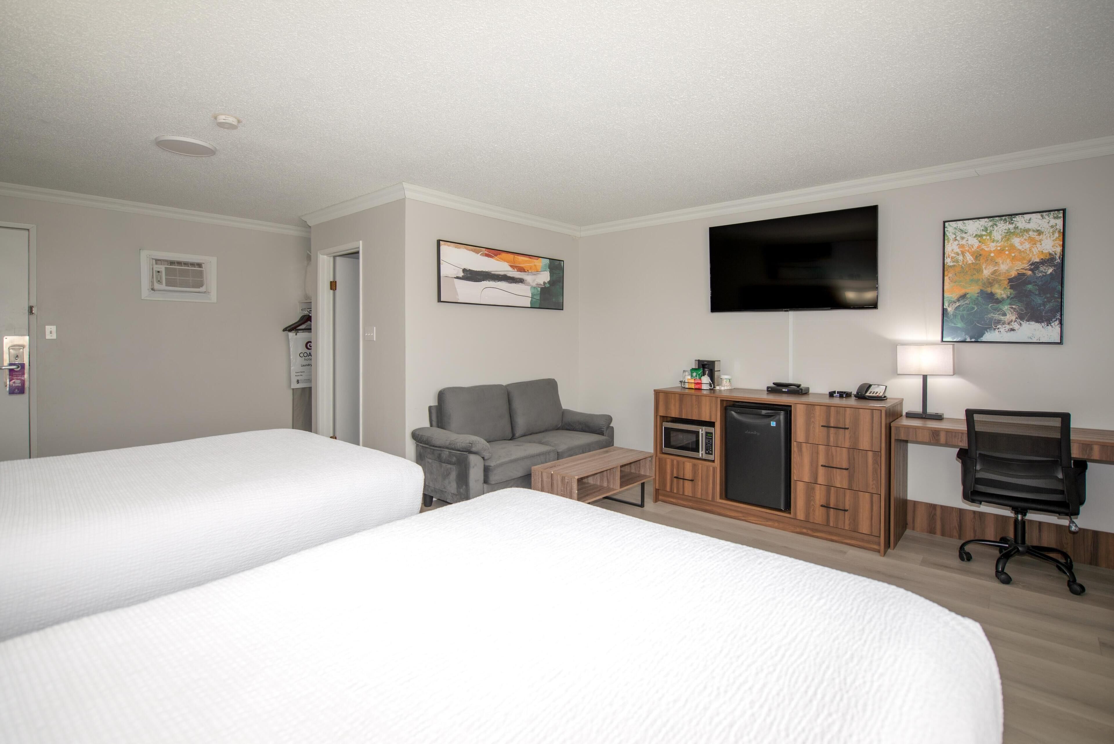 A hotel room with two beds, a sofa, a desk with a computer, a microwave, and a TV.