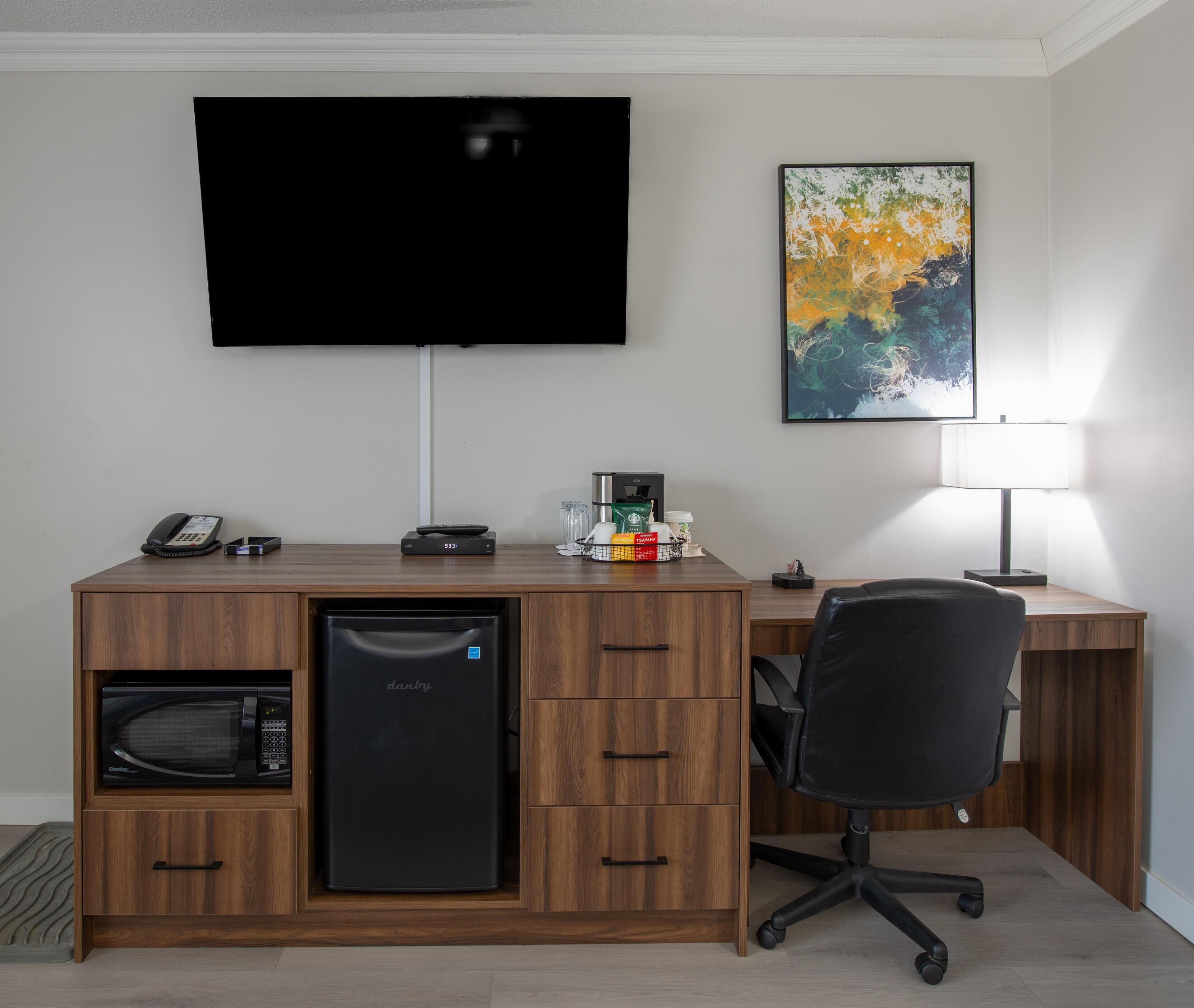 A hotel room with a flat-screen TV, a desk with a phone, a coffee maker, and a microwave.