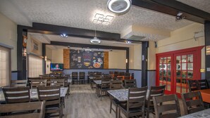 A restaurant interior with wooden tables and chairs, a menu board, and a red door.