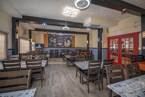 A restaurant interior with wooden tables and chairs, a menu board, and a red door.