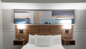 A hotel room with a large bed, wooden headboard, two bedside tables with lamps, and a wall-mounted artwork above the bed.