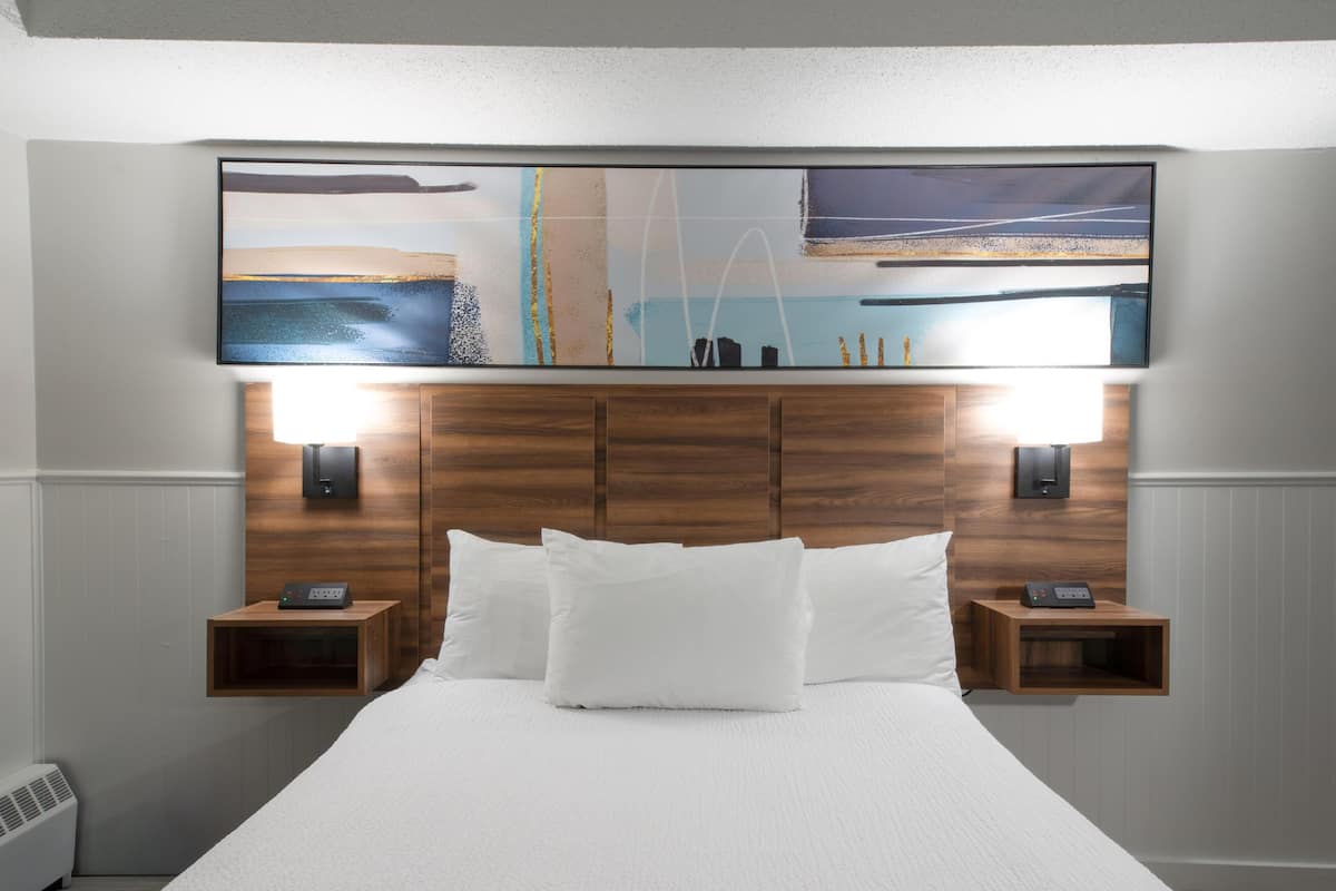 Ein Hotelzimmer mit einem großen Bett, einem Holzkopfstück, zwei Nachttischen mit Lampen und einem Wandbild über dem Bett.