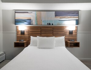 A hotel room with a large bed, wooden headboard, two bedside tables with lamps, and a wall-mounted artwork above the bed.