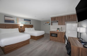 Habitación de hotel con dos camas, kitchenette, televisor de pantalla plana y obras de arte en las paredes.