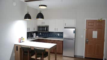 Una cocina moderna con armarios blancos, un refrigerador de acero inoxidable, un microondas y una mesa de comedor de madera con sillas.