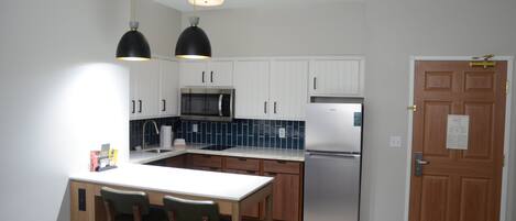 A modern kitchen with white cabinets, a stainless steel refrigerator, a microwave, and a wooden dining table with chairs.