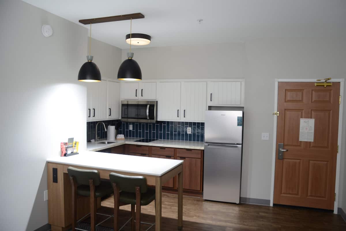 A modern kitchen with white cabinets, a stainless steel refrigerator, a microwave, and a wooden dining table with chairs.