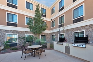 An outdoor patio with a round table and chairs, a grill, and a stone wall. - Staybridge Suites Tucson Airport by IHG (Tucson)