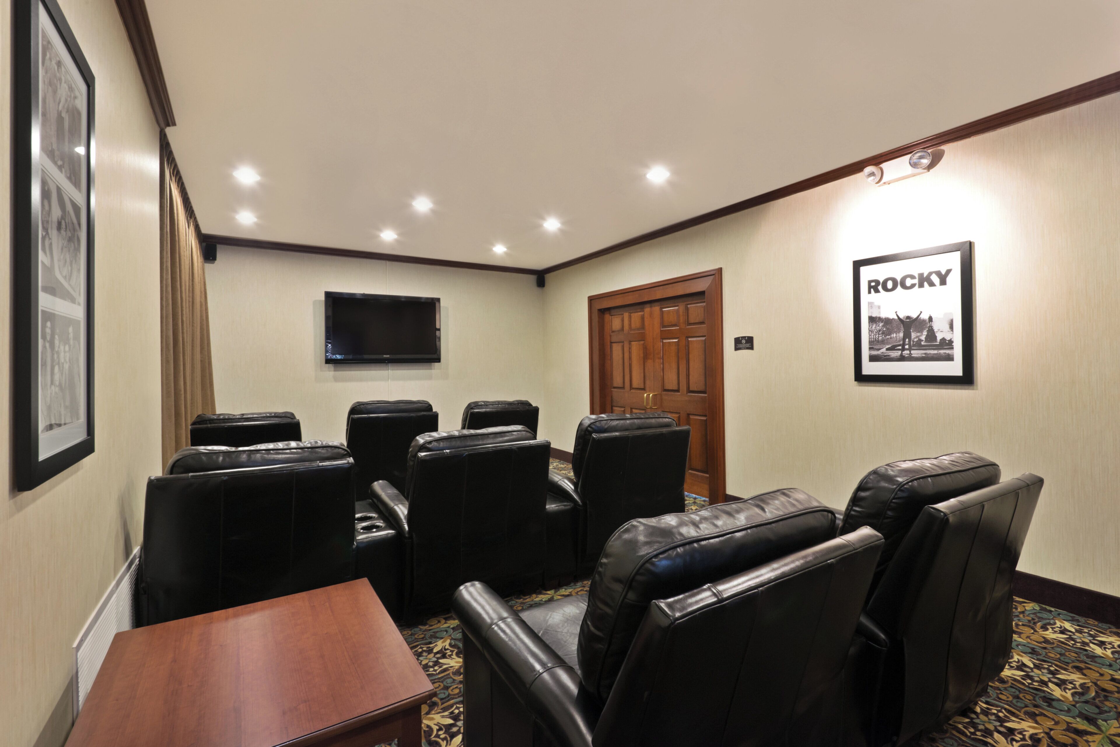 A conference room with a wooden table, black leather chairs, a mounted flat-screen TV, and a framed picture on the wall.