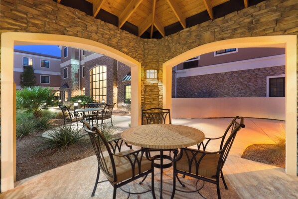 An outdoor patio with a round table and chairs, surrounded by stone walls and a view of adjacent buildings.