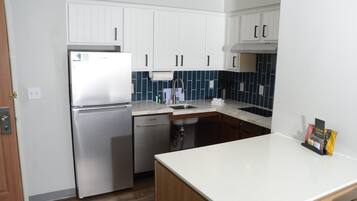 A compact kitchen with white cabinets, a stainless steel refrigerator, a dishwasher, and a tiled backsplash.