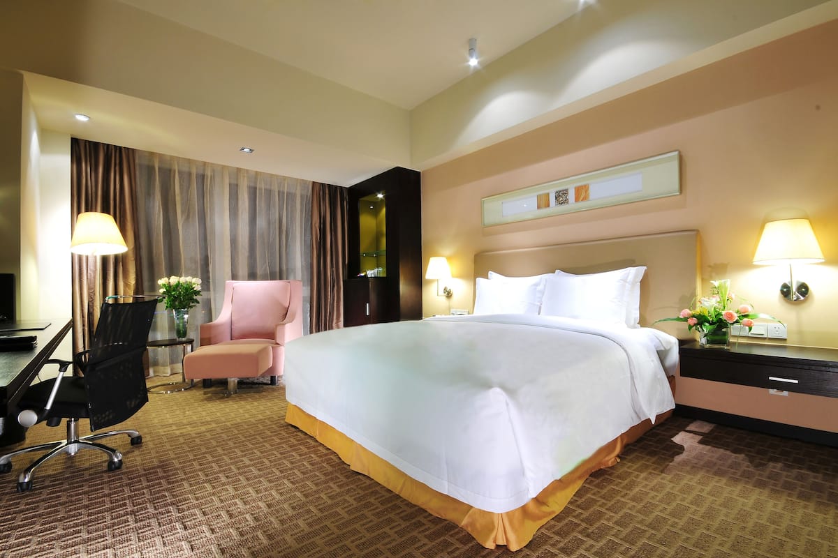 Ein Hotelzimmer mit einem großen Bett, einem Schreibtisch mit Stuhl, einem kleinen Tisch mit Blumenvase und zwei Wandleuchten.