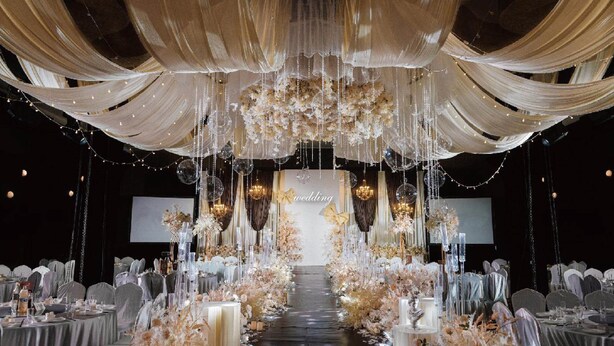 Une salle de réception où les tables sont dressées pour un banquet de mariage, recouvertes de tissu blanc et décorées de compositions florales.