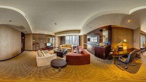 Un hall d’hôtel spacieux doté d’un plafond incurvé, d’un coin salon avec des canapés et une table basse, d’un téléviseur, ainsi que d’un bar avec un comptoir et des chaises.
