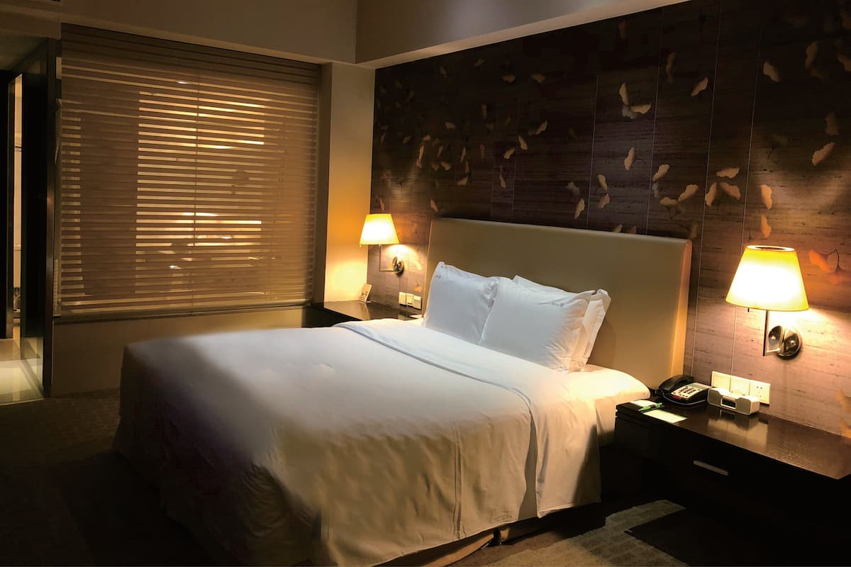 Ein Hotelzimmer mit einem großen Bett, zwei Nachttischlampen, einem Holzkopfschild und einem Fenster mit Jalousien.