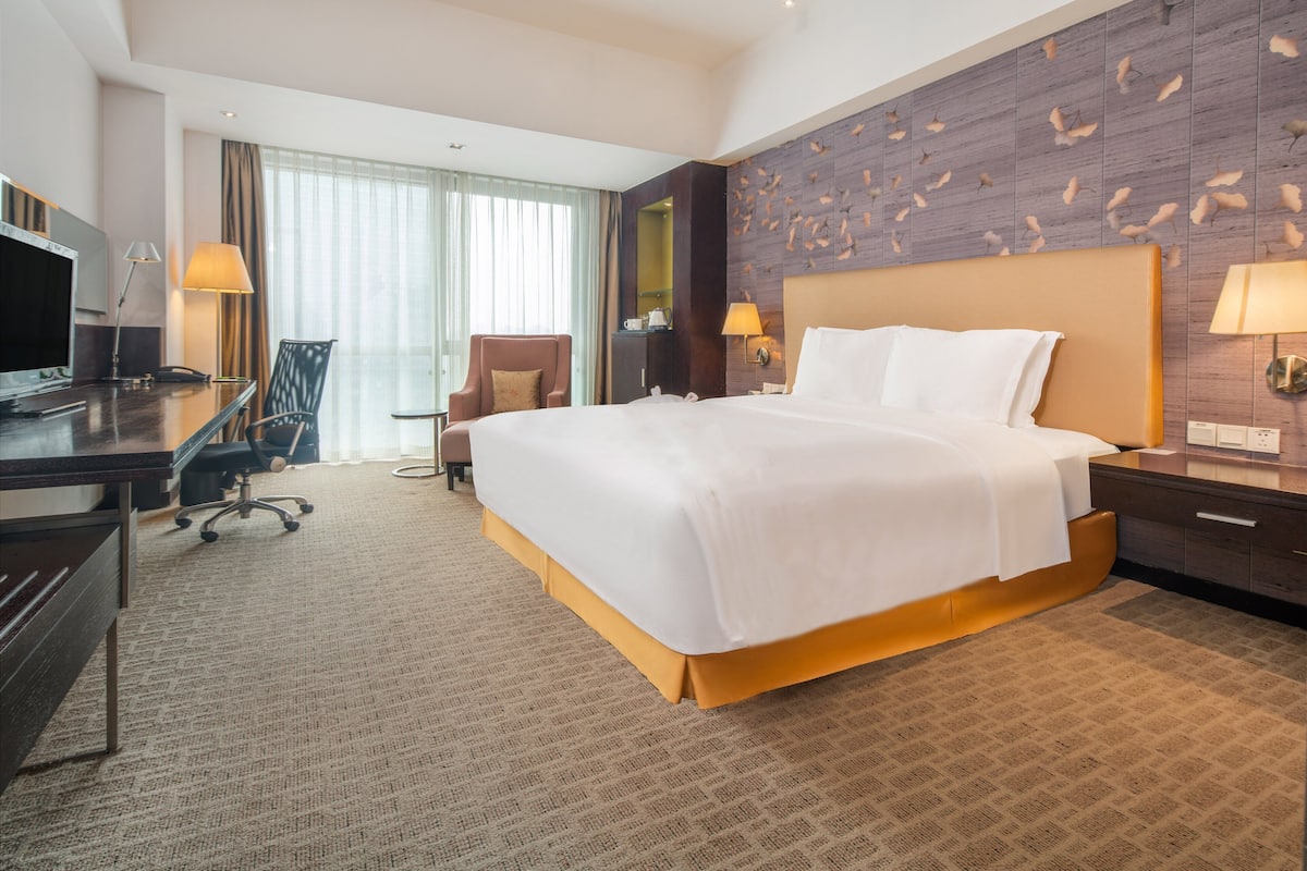 Ein Hotelzimmer mit einem großen Bett, einem Schreibtisch mit Computer, einem Sessel und einem Fernseher.