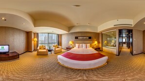 Une chambre d’hôtel spacieuse, dotée d’un grand lit, de deux fauteuils, d’un bureau et d’une salle de bain fermée par des parois de verre.