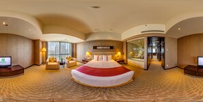 Ein geräumiges Hotelzimmer mit einem großen Bett, zwei Sesseln, einem Schreibtisch und einem Glaskastenbad.