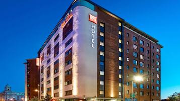A hotel with a modern design, featuring a prominent 'Ibis Hotel' sign, multiple floors, and a corner location.