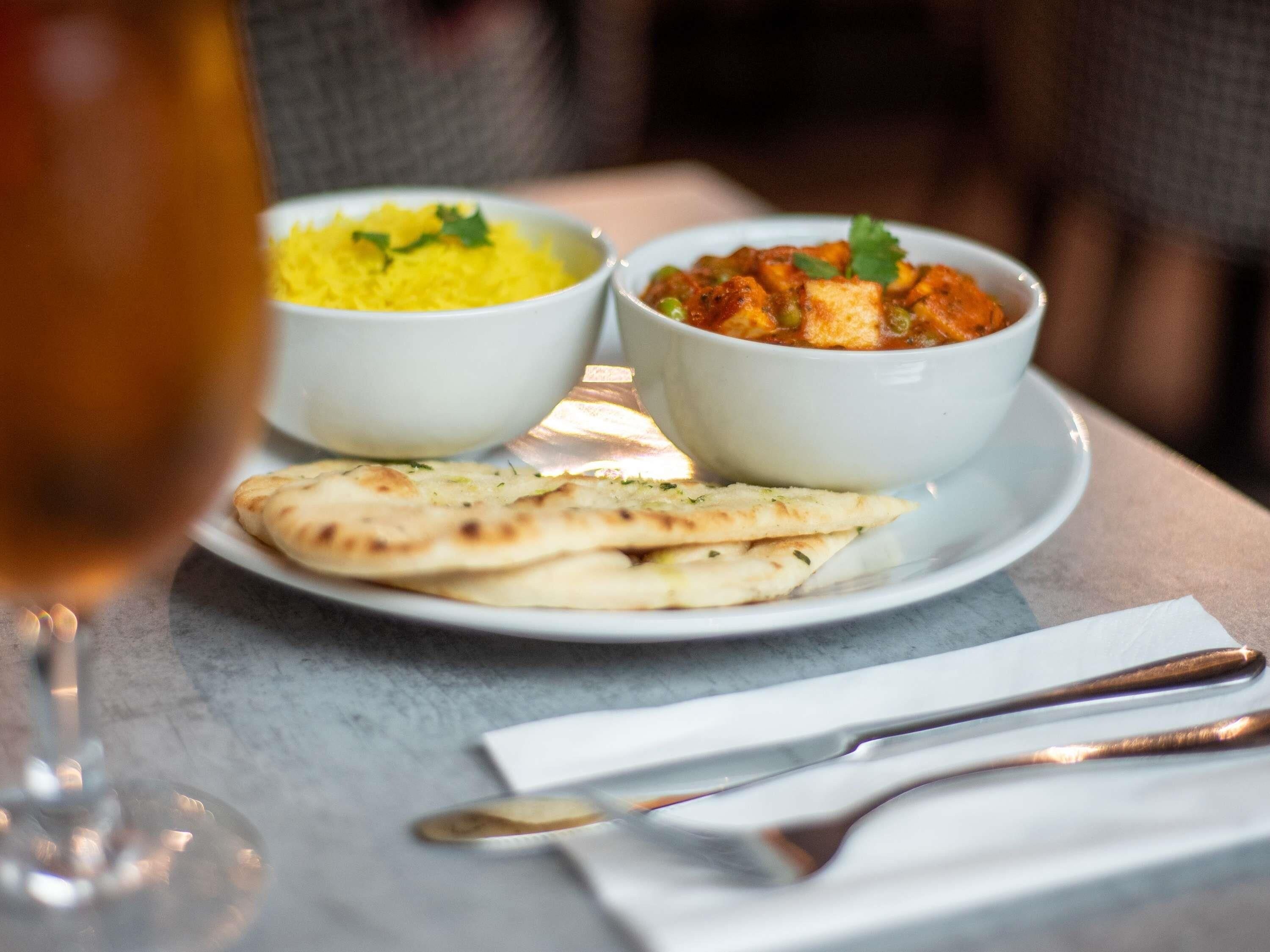 A plate with two bowls of food, a glass of a yellow beverage, and flatbread on a table.