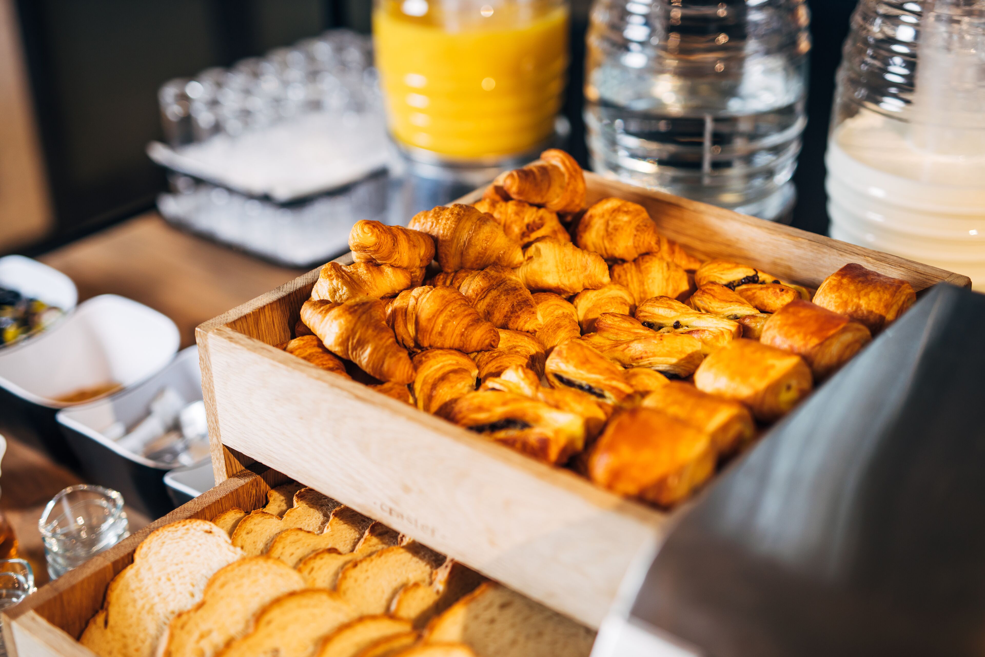 A breakfast buffet with croissants and bread, juice, and milk.