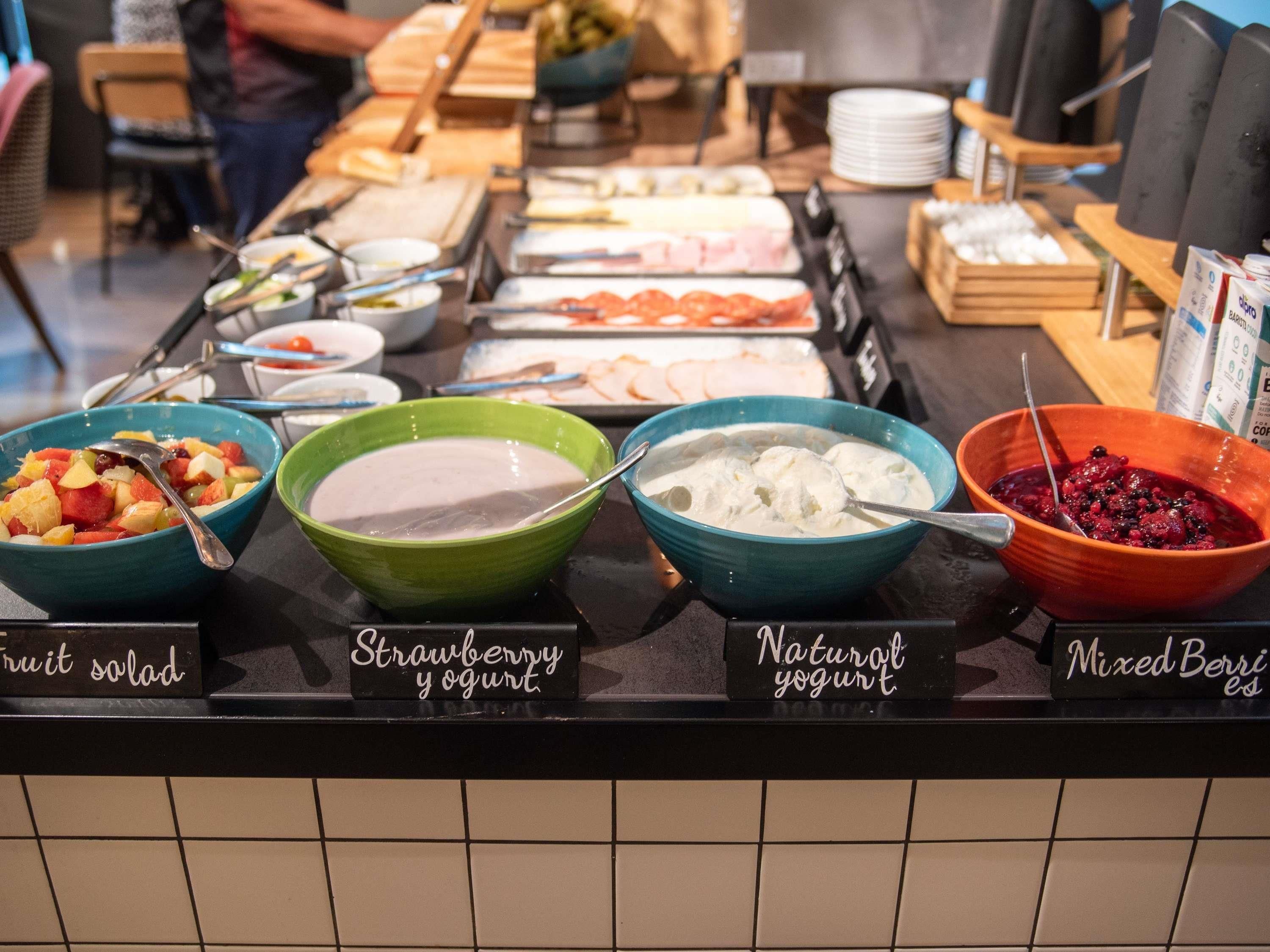 A buffet with labeled bowls of fruit salad, strawberry yogurt, natural yogurt, and mixed berries.