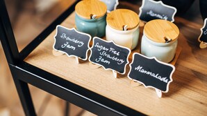 A selection of jars labeled with different types of jam on a wooden tray. - ibis Belfast City Centre (Belfast)