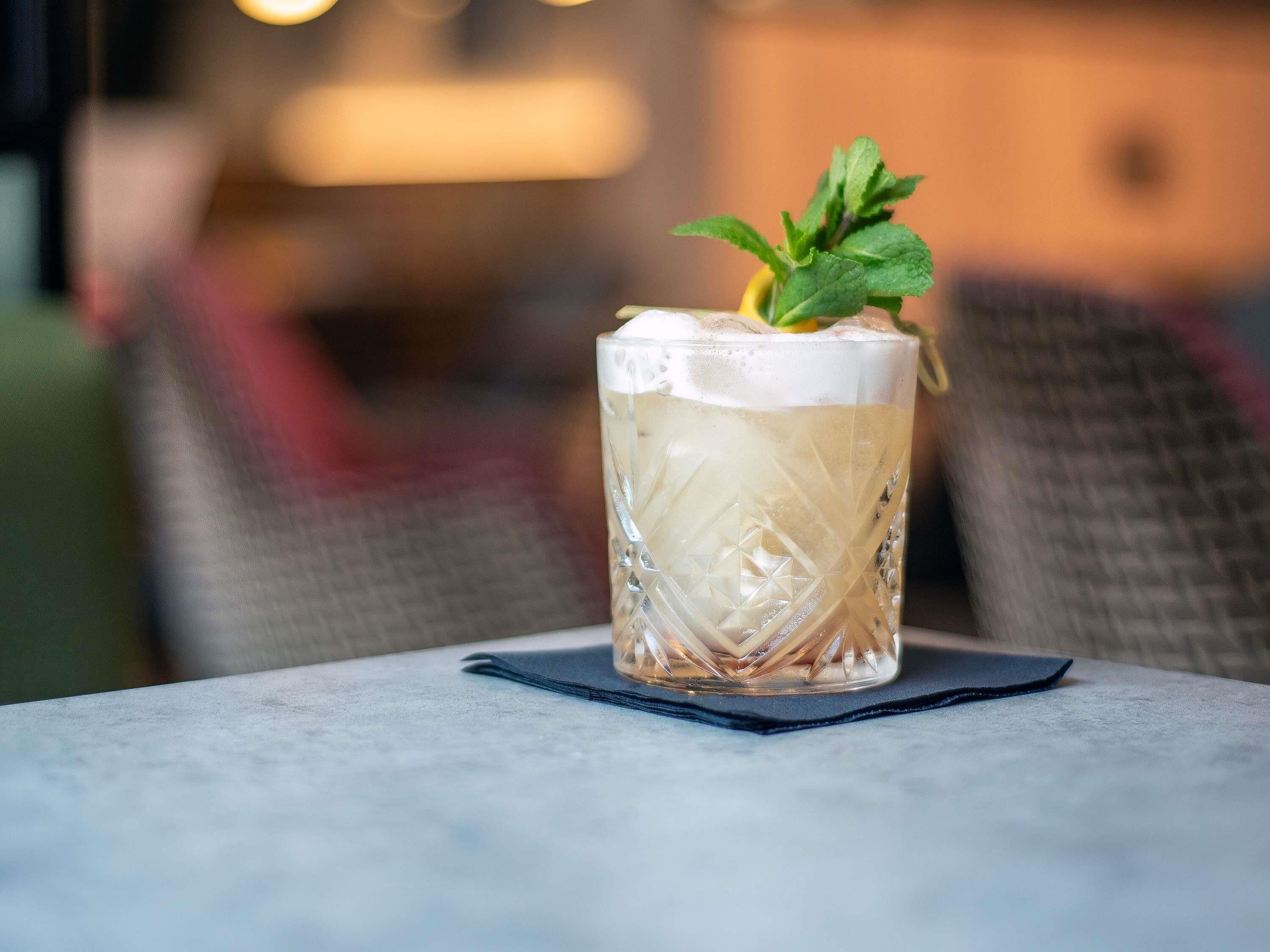 Un verre transparent, décoré d’une feuille de menthe, est posé sur une table.