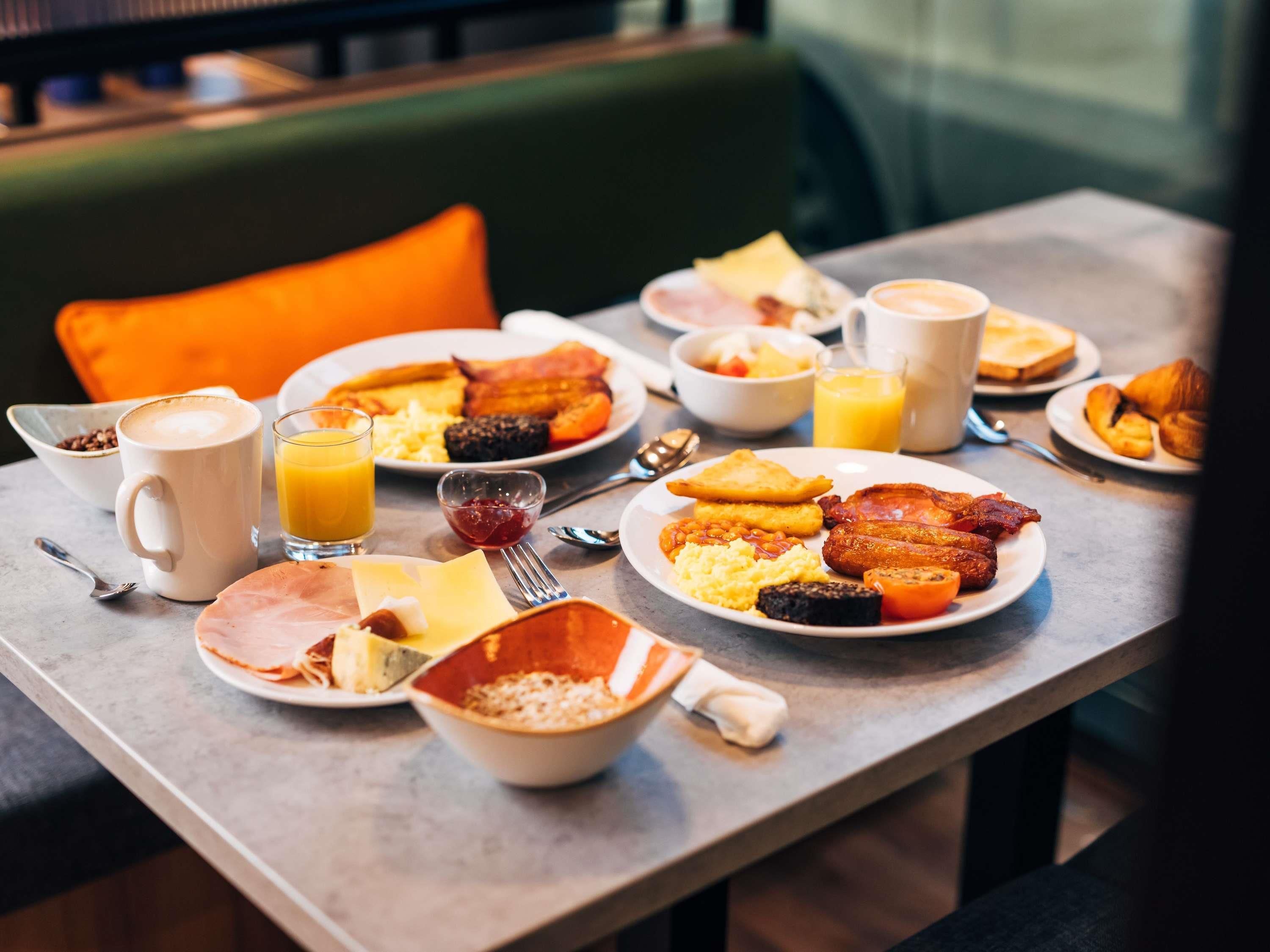 A breakfast table with plates of food, a coffee cup, and a glass of orange juice.