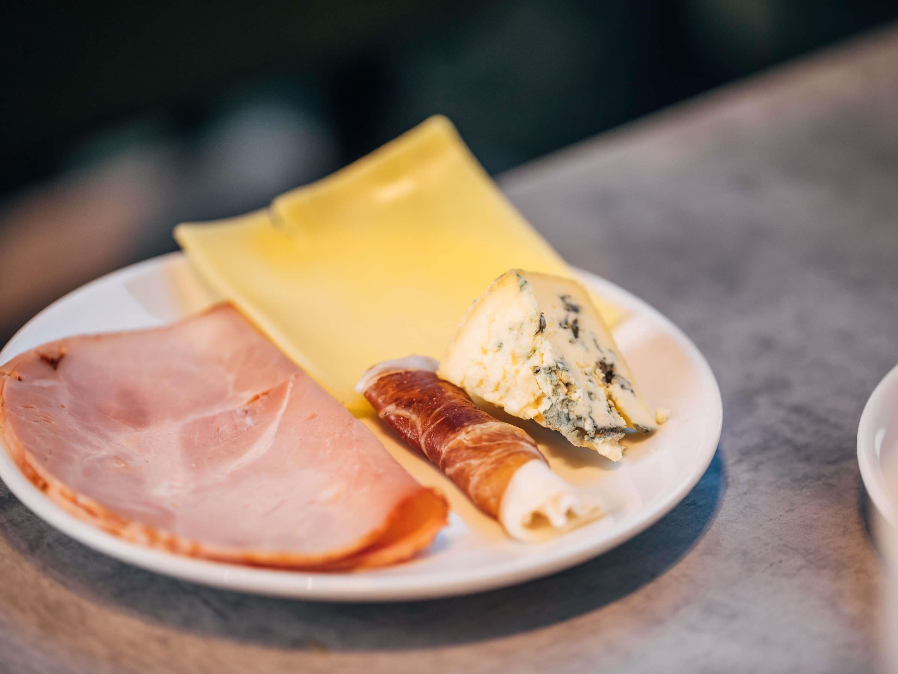A plate with slices of ham, a piece of cheese, and a rolled pastry.