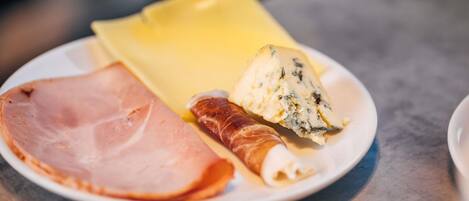 A plate with slices of ham, a piece of cheese, and a rolled pastry.